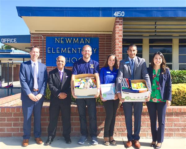 Six adults -- four men and two women -- holding school supplies in front of an elementary school. Six adults -- four men and two women -- holding school supplies in front of an elementary school.